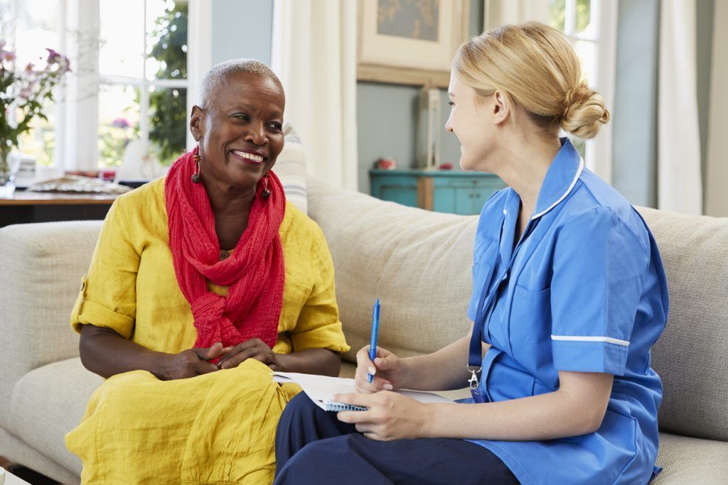 A care professional speaking with an older woman seated in her home